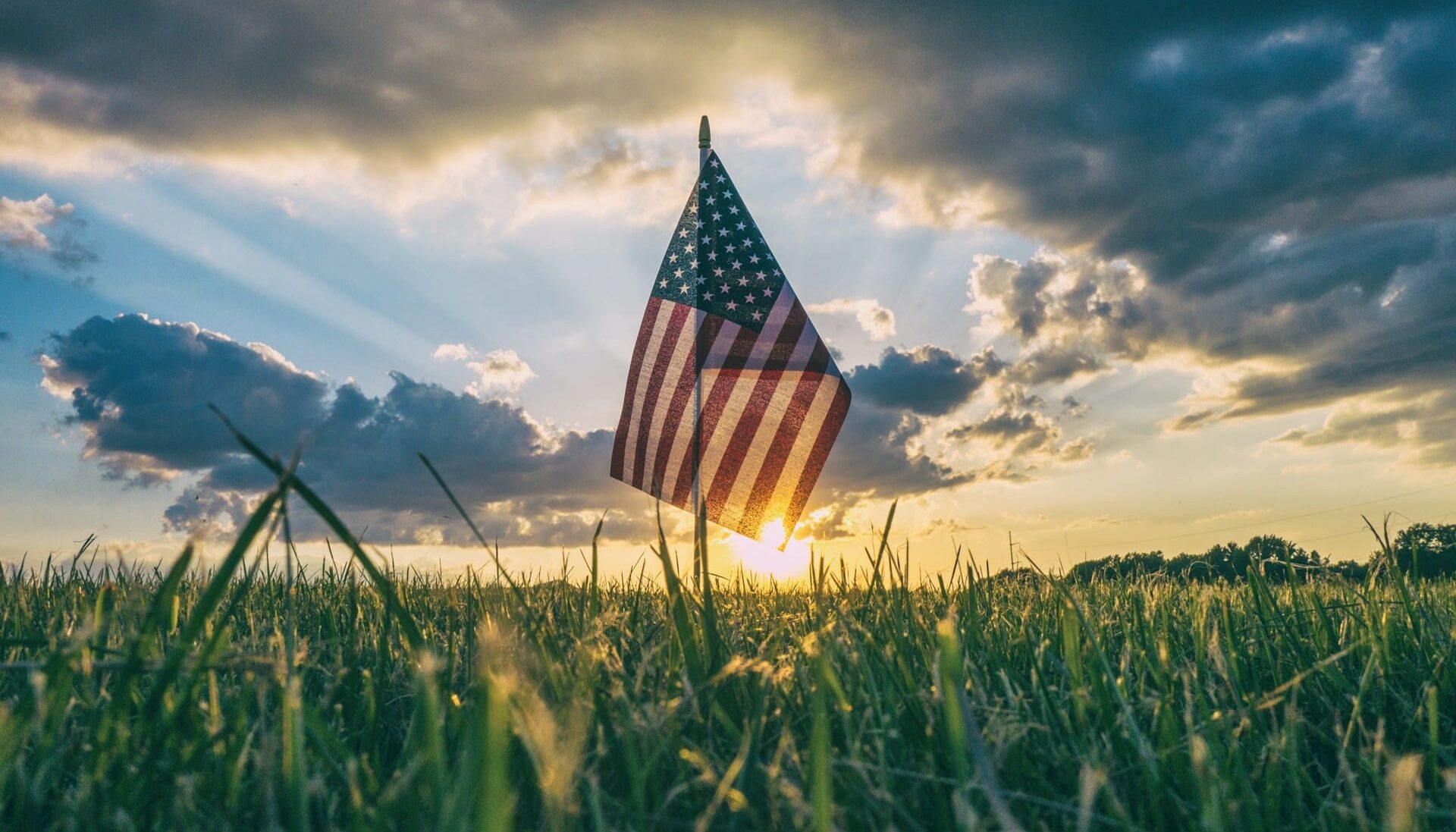 Close-up of an American flag planted in a grassy field at sunset, representing US border crossing issues