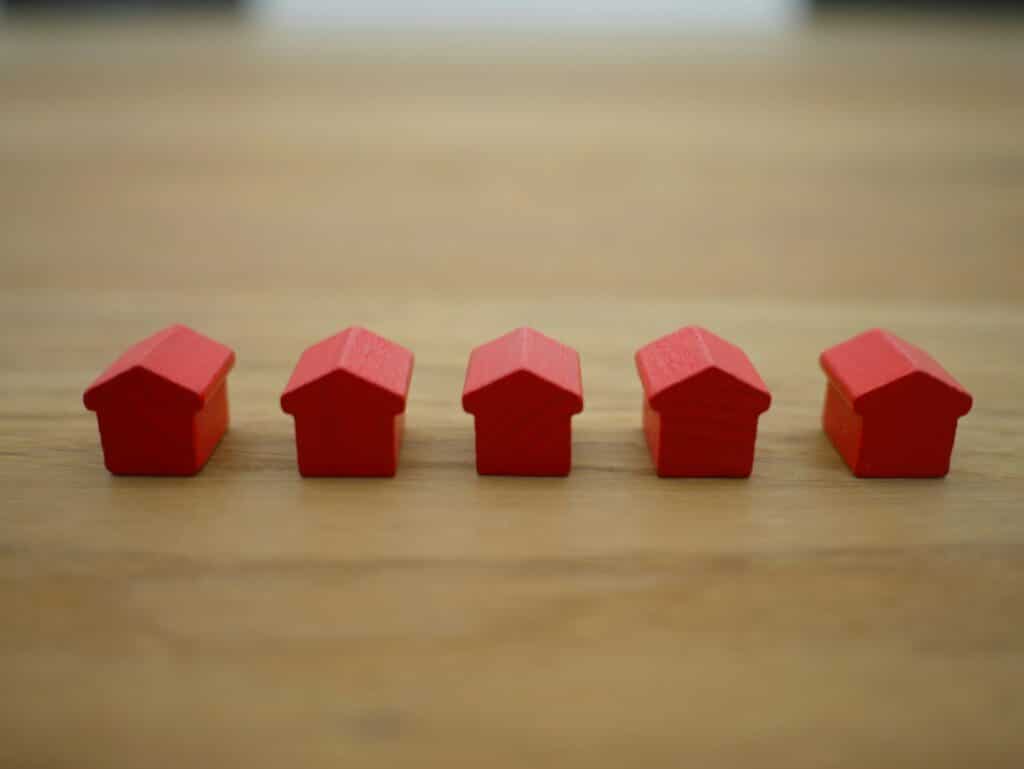 A line of five small, red wood houses set on a wooden tabletop, representing real estate incentive clauses.