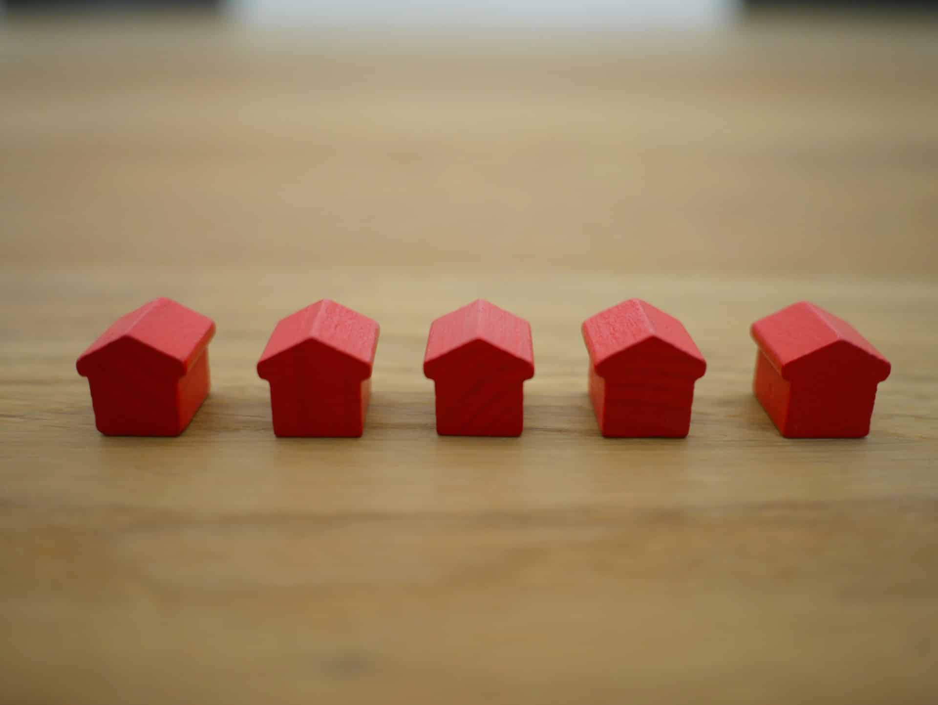 A line of five small, red wood houses set on a wooden tabletop, representing real estate incentive clauses.