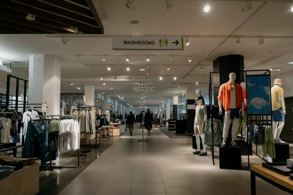 A department store with racks of clothes to the left of a wide tile aisle and a group of faceless mannequins in various poses on the right, and two people walking away down the aisle, similar to the property discussed in the blog and representing commercial tenant lease breaks.